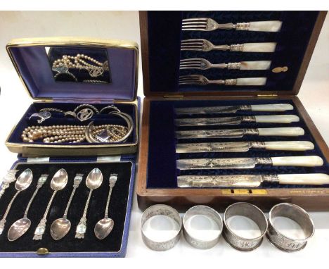 Four silver napkin rings, jewellery, plated souvenir spoons and a mother of pearl handled plated knife and fork set in wooden