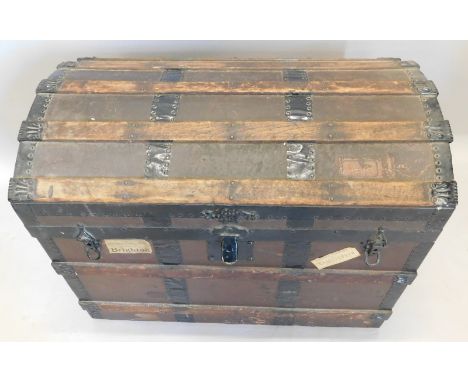 An early 20thC ebonised metal, wooden and canvas bound dome top trunk, with side handles, various luggage labels etc.