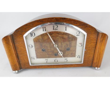 An Art Deco style oak mantel clock, the part silvered dial with an arched chrome plated bezel, striking on the hour and with 