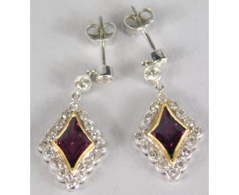 A pair of ruby and diamond earrings, with central diamond shaped ruby, surrounded by tiny diamonds, with a single round brill