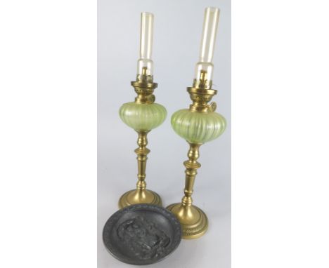 A pair of early 20thC brass and glass candlestick lamps, with green glass reservoirs on turned circular stems and shaped feet