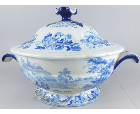 A 19thC blue and white pottery tureen, decorated with figures and houses, on a shaped foot with moulded shell handles and an 