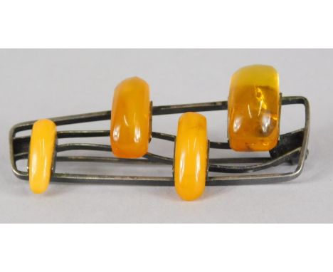 A Russian butterscotch amber brooch, with four amber beads, two butterscotch, two lighter orange in colour, on white metal ba