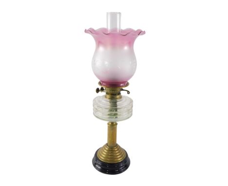 A Victorian brass oil lamp, with clear glass reservoir, ceramic base and later cranberry tinted shade. 