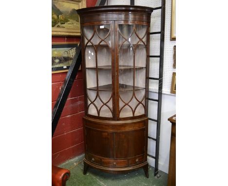 A mahogany bowfront floor standing corner cabinet, stepped cornice, two astragal glazed doors enclosing shelving to top, two 