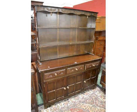 An oak dresser, two shelves to top, three carved front short drawers over three panelled door cupboard to base.