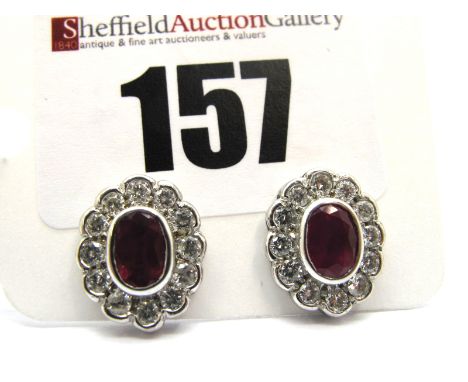 A Pair of Modern Ruby and Diamond Oval Cluster Earstuds, oval collet rubover set to the centre within border of brilliant cut