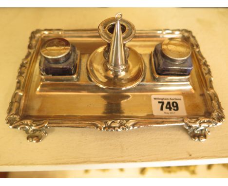 A silver plated desk stand of two inkwells, chamber stick with snuffer raised on foliate scroll feet