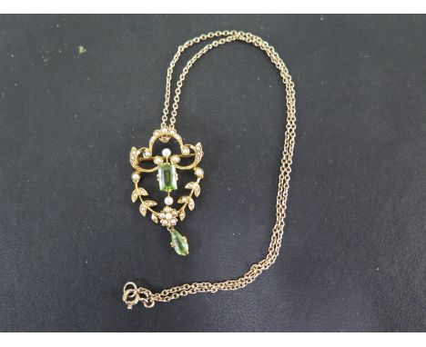 A yellow gold pendant, scroll top with floral and leaf, articulated swag below, set throughout with seed pearls and an emeral