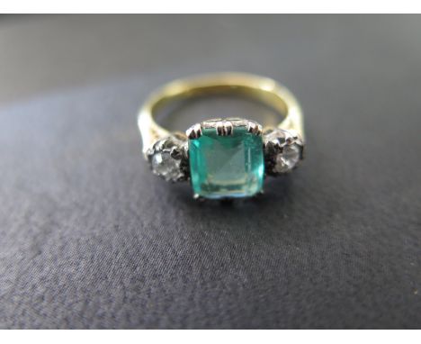 An emerald and diamond 18ct gold and diamond ring, the centrally set emerald measures approx. 7mm x 7mm is flanked by two dia