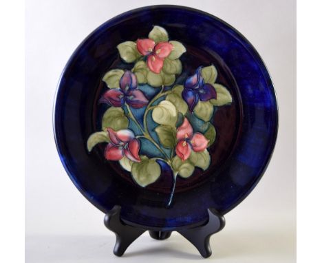 Two Moorcroft plates one with 'Orchid' pattern and the other the 'Bougainvillea' pattern, over navy blue ground, signed and i