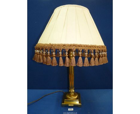 A brass column lamp with large cream shade having gold coloured tassels.