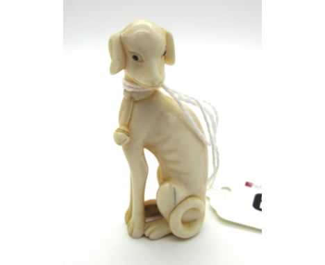 A XIX Century Japanese Ivory Netsuke, carved as a seated dog with his head turned to the left, wearing bells which hang from 