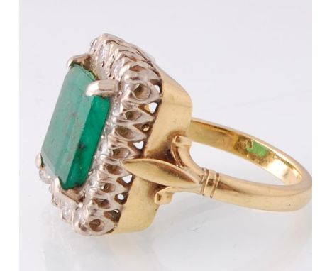 An 18ct yellow and white gold emerald and diamond cluster ring. The central trap cut, 4 claw set emerald ( 11 x 9.7mm / est 3