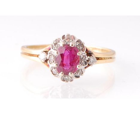 An 18ct gold, ruby and diamond cluster ring.&nbsp; The central oval cut ruby approx 6mm x 4mm within a halo of brilliant cut 