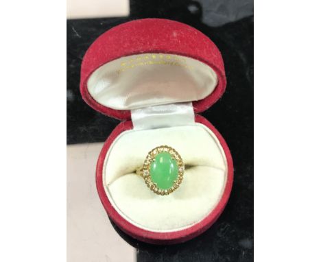 An 18 carat gold mounted dress ring set with cabouchon cut jade of oval form flanked by two small diamonds, size L/M, 4 g ove