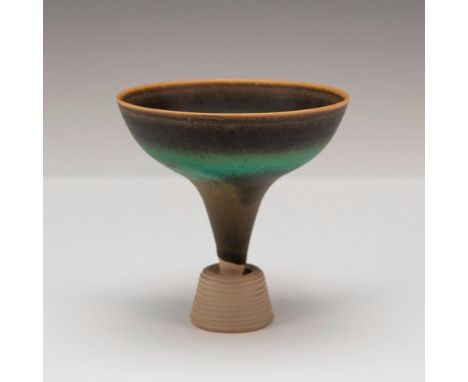 A green mottled glazed funnel form vase with black, blue, and amber speckles, and a ridged base. Gustavsberg stickered. Artis