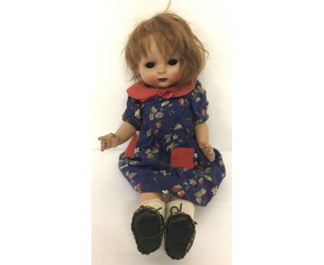 A vintage composition walking doll with painted face and closed mouth in blue floral dress. Eyes need attention.