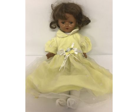 A vintage composition doll with jointed body and closing eyes. Open mouth with red painted lips in a pale yellow dress.