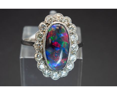 A PLATINUM, BLACK OPAL AND DIAMOND RING, the oval cut opal set within a scalloped mount of brilliant cut diamond highlights b