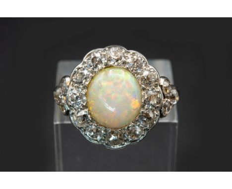 AN OPAL AND DIAMOND RING, the round cut opal set within a scalloped edge surround of old brilliant cut diamonds between diamo