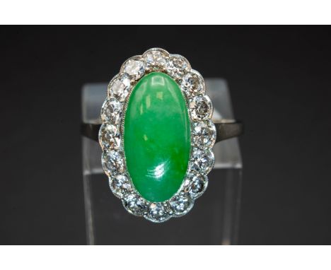 A JADE AND DIAMOND RING, the oval cabochon cut jade set within a surround of brilliant cut diamonds in a scalloped edge mount