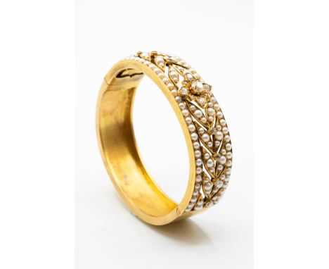 A SEED PEARL AND DIAMOND BANGLE, the pierced detail mount of leaf design set throughout with seed pearls, with central flower
