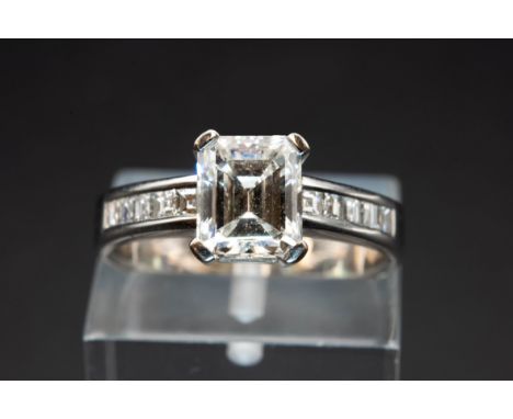 A DIAMOND AND WHITE GOLD RING, the rectangular cut diamond claw set between square cut diamond set shoulders. Stamped 750. Ri