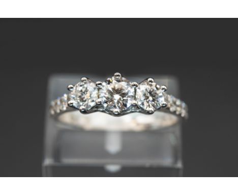 A THREE STONE DIAMOND RING, the three graduating brilliant cut diamonds set between further brilliant cut diamond highlights 