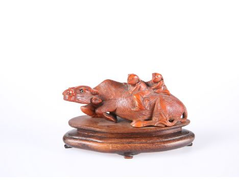 A CHINESE CINNABAR LACQUER MODEL OF A BUFFALO, modelled with two children on its back, with glass eyes and mounted on a shape