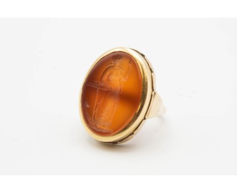 A 9CT YELLOW GOLD AND CARNELIAN INTAGLIO RING, the oval carnelian mount carved to the centre with maiden in robes, standing w