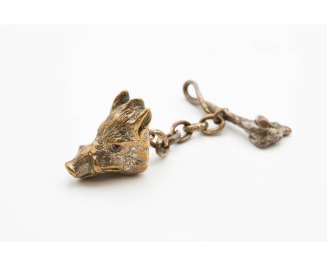 A WHITE METAL HUNTING CLOAK CLASP, modelled as a boar's head with red glass inset eyes linked by a chain to a whip with dog's