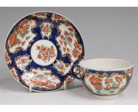 A Dr Wall period Worcester porcelain teacup and saucer, decorated with reserves in the Imari palette on a blue scale ground, 