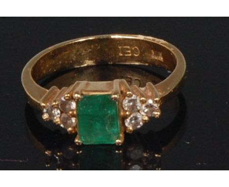 A modern 18ct gold, emerald and diamond dress ring, the central square cut emerald flanked to either side with three small cl