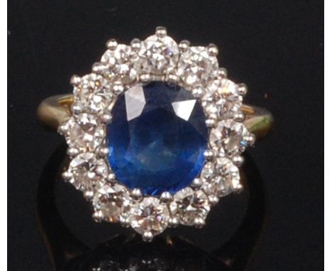 An 18ct gold, sapphire and diamond cluster ring, the central claw set oval cut sapphire weighing approx 2.9ct, within a surro