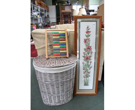 A glazed and framed poppy tapestry with a child's abacus and a woven wicker laundry basket.