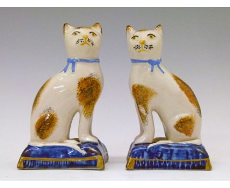 Pair of Staffordshire figures, each depicting a seated cat with tortoiseshell patch decoration, seated on a gilt highlighted 