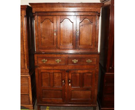 An antique oak livery cupboard, the upper section surmounted by a stepped canopy above cupboards, two drawers below, lower sh