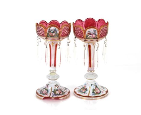 A pair of Victorian overlaid ruby glass lustre vases having floral decoration heightened in gilt, hung with glass prism drops