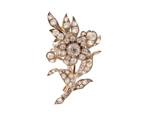 A stylised diamond set spray brooch, the central flower head cluster surrounded by scroll and leaf designs,  comprising round