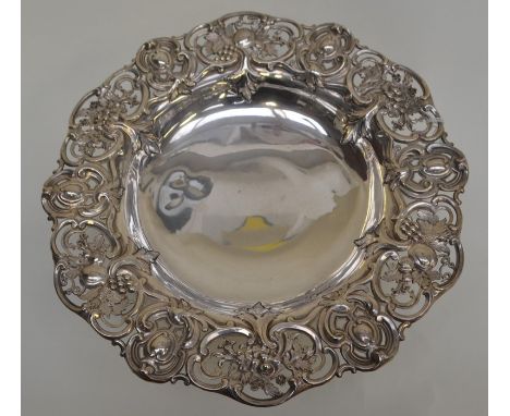 An Edwardian silver circular raised dish, the sides chased with fruit and foliage with openwork scrolls, on trumpet shaped fo