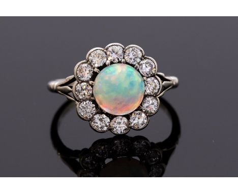 An Art Deco opal and diamond ring, the round cabochon opal set centrally with a milled border of old cut diamonds, split shou