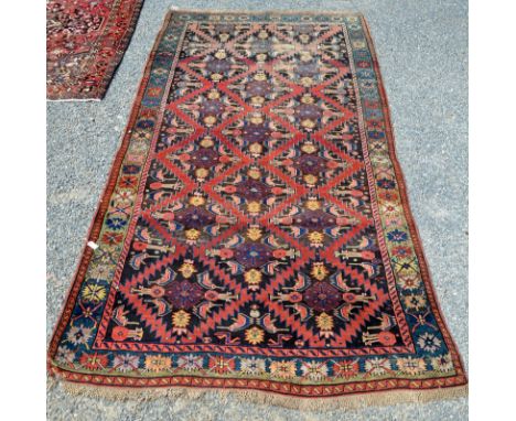 An eastern hand knotted carpet, the red ground filled with stepped medallions within a flowerhead border. 203 x 434cm. Condit