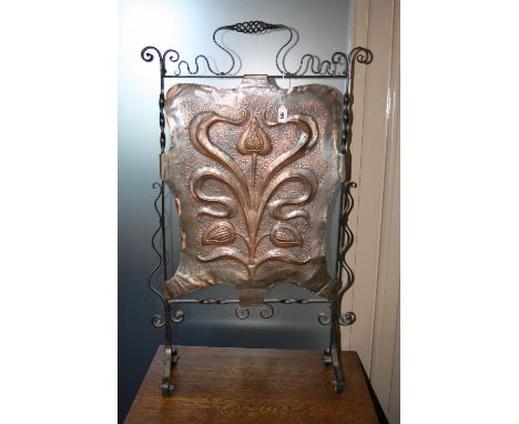 A WROUGHT IRON FRAMED FIRE SCREEN, having central beaten copper panel with stylised floral relief decoration, shaped frame, s