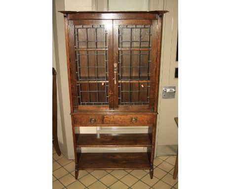 AN OAK ARTS & CRAFTS STYLE CABINET, having glazed leaded double doors to three shelf interior over long drawer with copper ri