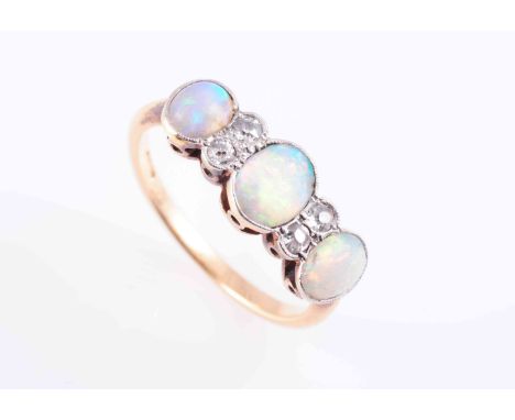 AN OPAL AND GOLD RING, CIRCA 1900, the central oval cut opal collet set between two old brilliant cut millegrain set diamond 