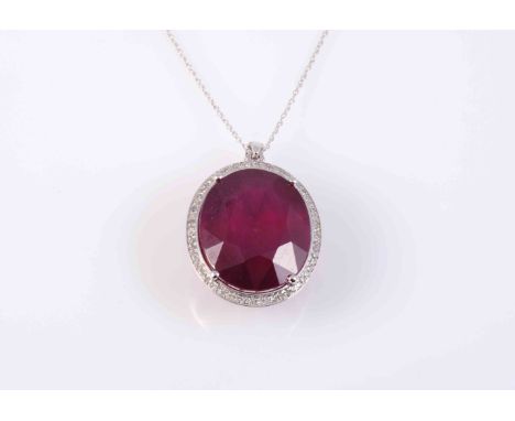 A RUBY AND DIAMOND PENDANT, the large oval cut ruby four claw set within a surround of brilliant cut diamond highlights, all 