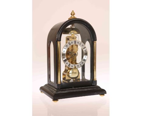 A FRANZ HERMLE EBONISED MANTEL CLOCK WITH SKELETON MOVEMENT, the case with arched top, turned brass finial and gilded columns