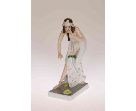A ROSENTHAL FIGURE OF A SEMI-NUDE FEMALE SNAKE CHARMER, c.1920, bending down over a small green Cobra and playing a pipe, pri