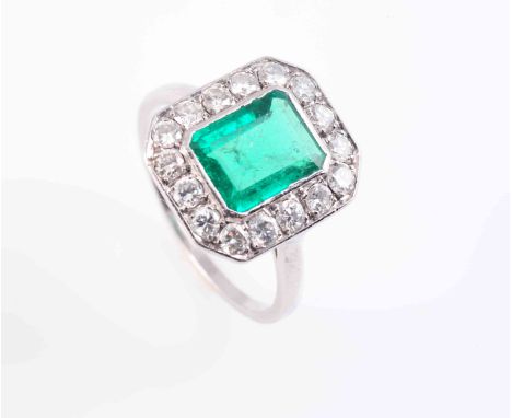 AN EMERALD AND DIAMOND RING, the rectangular cut emerald collet set within a surround of sixteen brilliant cut claw set diamo